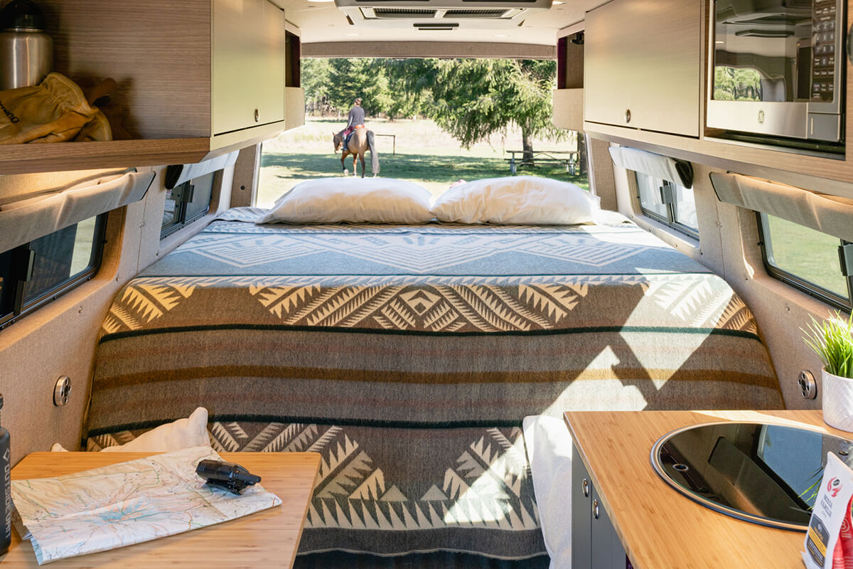 Three panel raised bed with one panel folded down into a sofa, back doors open with a horseback rider in the distance