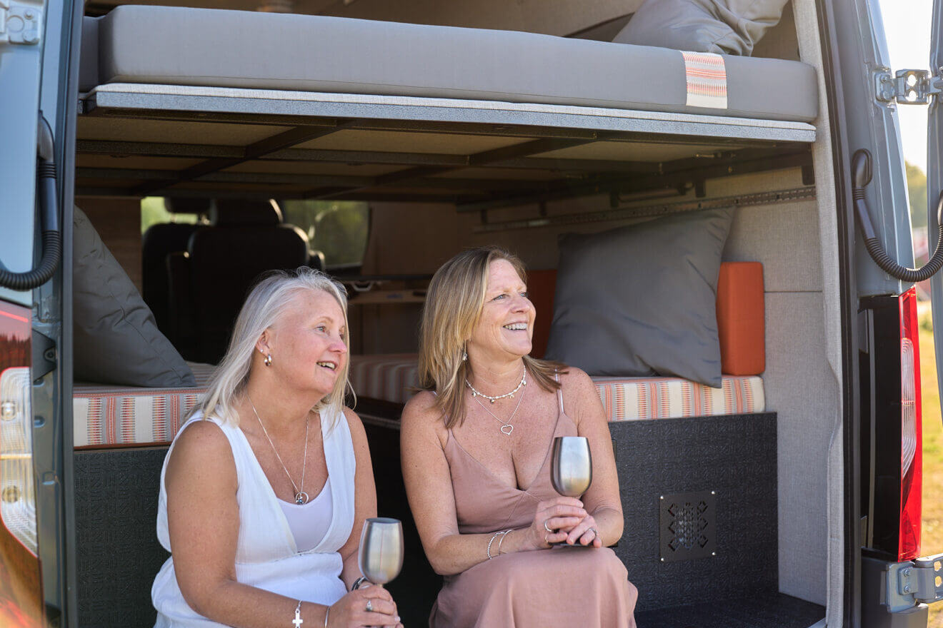 Two ladies sitting on the bumper of a custom van, enjoying the view