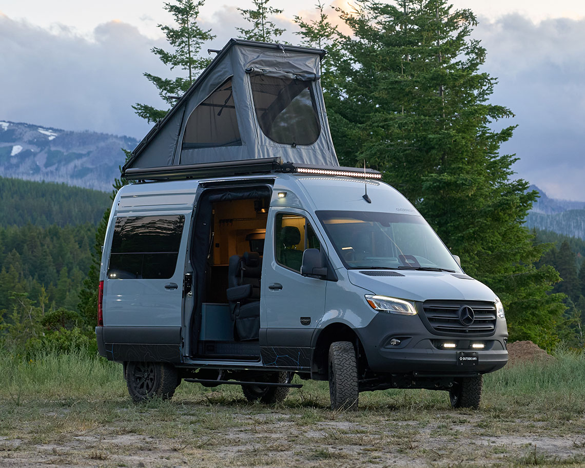 Outside Van Overnight with rooftop tent deployed in a forest mountain scene.