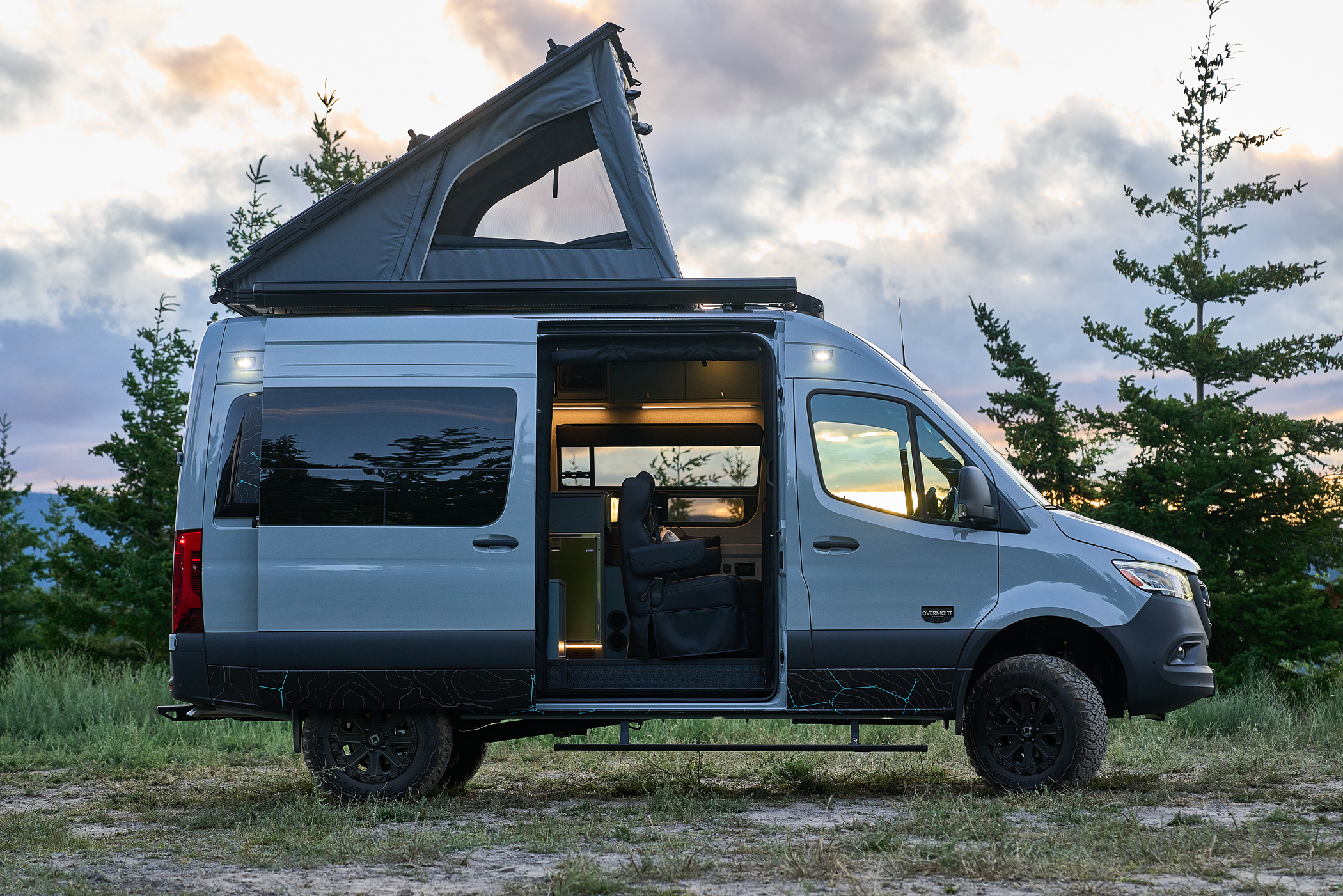 Outside Van Overnight with pop-up roof tent deployed in a forest scene at sunset or sunrise.