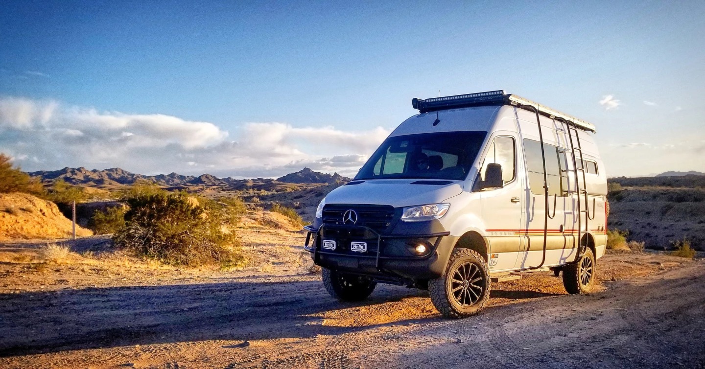 Storyteller Overland mode van in a desert scene with headlights on.