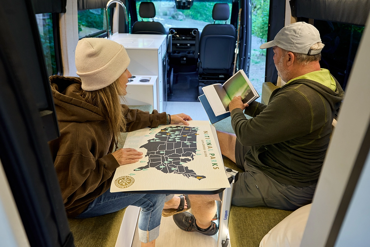 Couple looks at national park map while sitting at dinette table in Outside Van Parks model