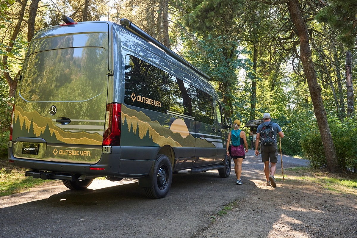 Couple walking to the trailhead next to a Parks model from Outside Van